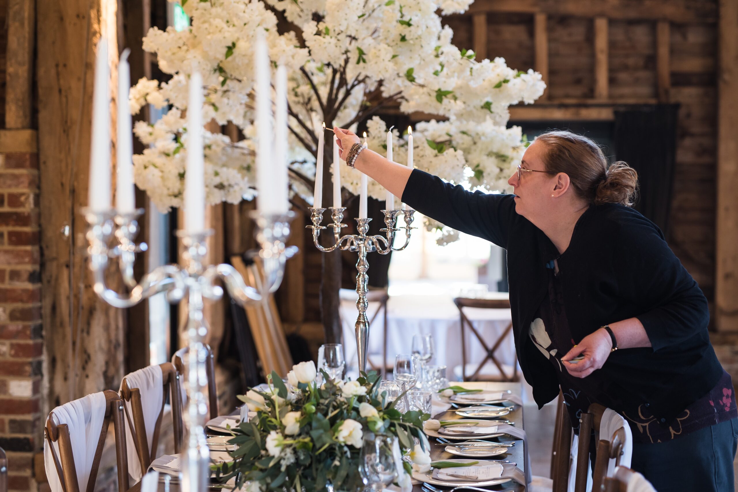 Your Wedding Friend is lighting some candles on silver candlesticks with a white blossom tree in the background