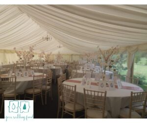 White Marquee set up with wedding breakfast tables with white cloths and white blossom trees on each table