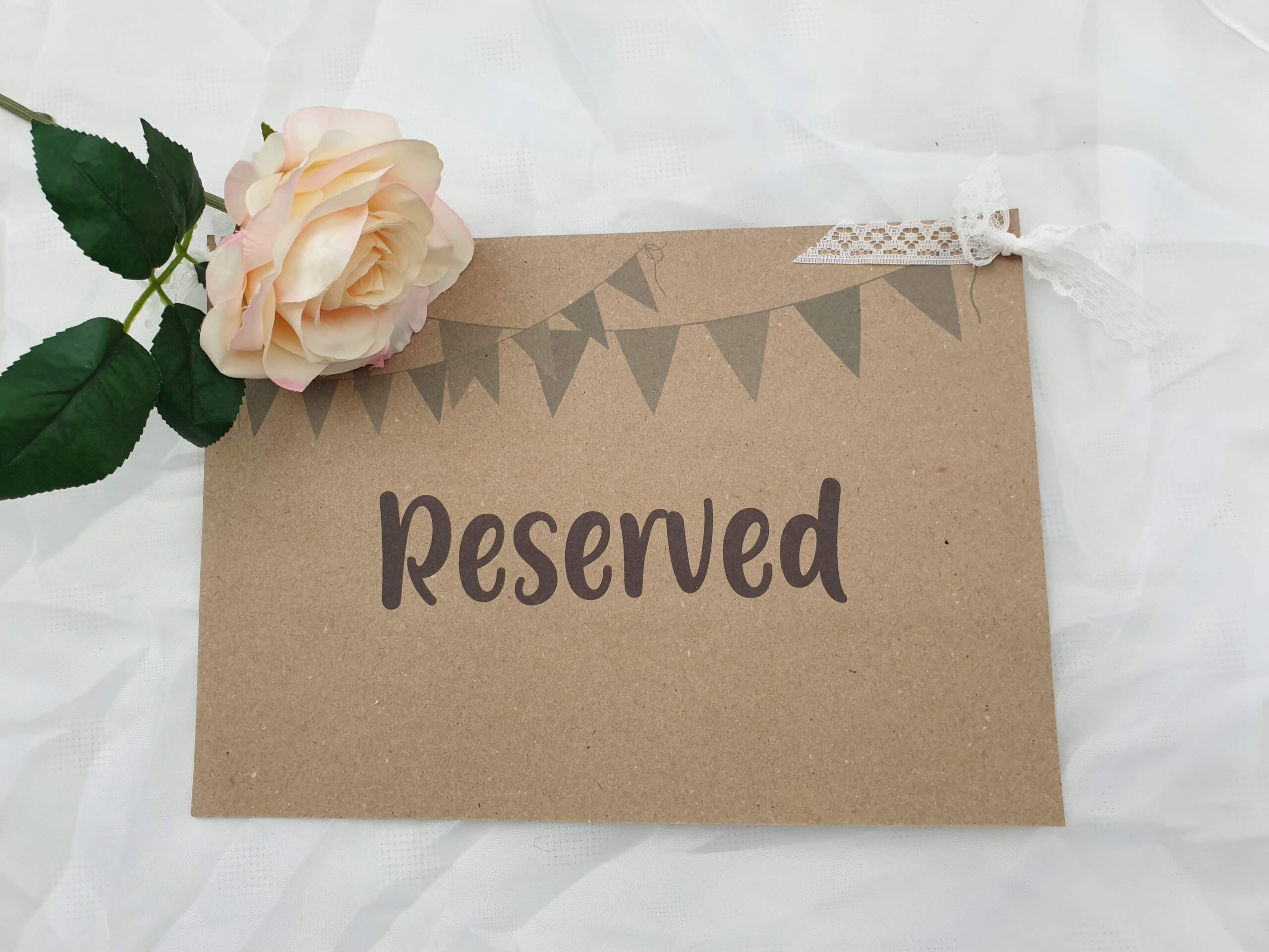 A rustic card has the word reserved printed on it with a cream rose placed on it at the top left