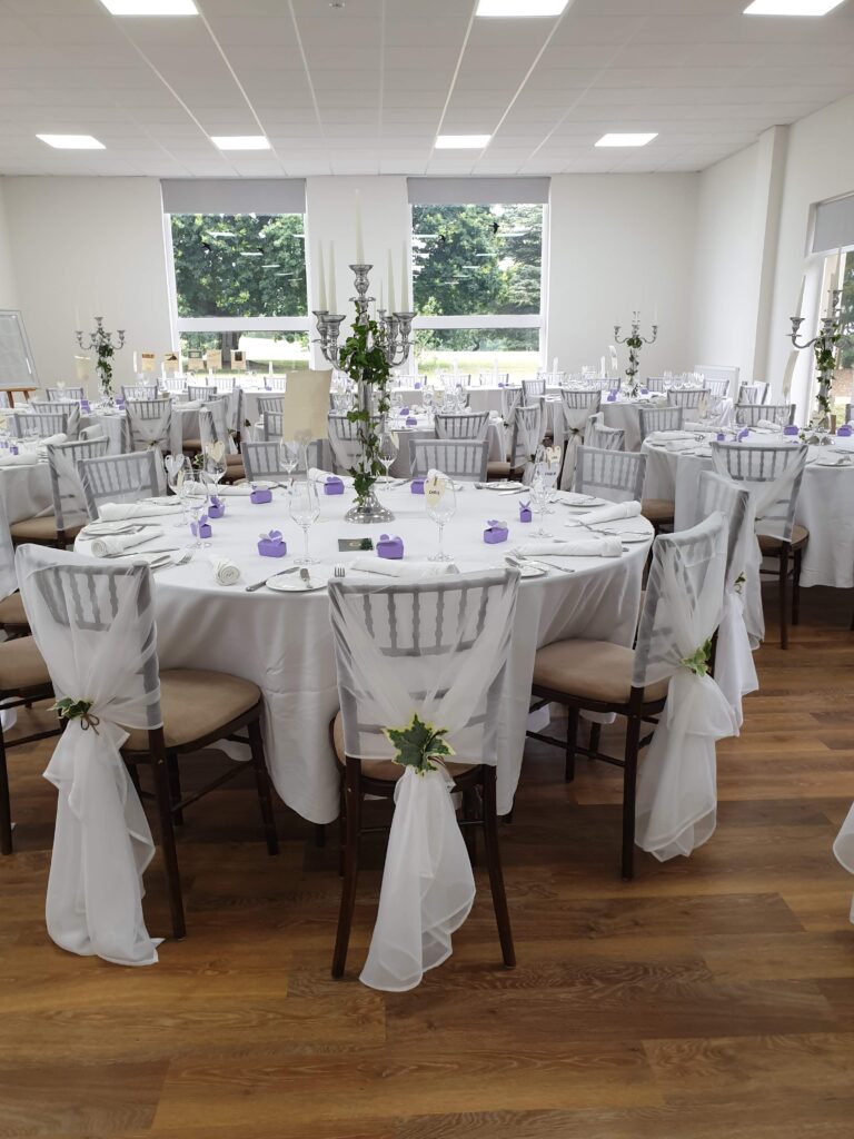 a white room with a dressed white tables is ready for a wedding breakfast