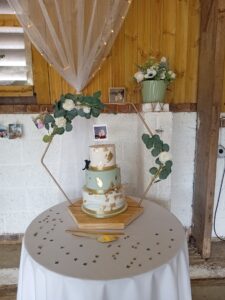 a three tier white and sage green wedding cake deocrated with gold leaf and on a hexagonal stand