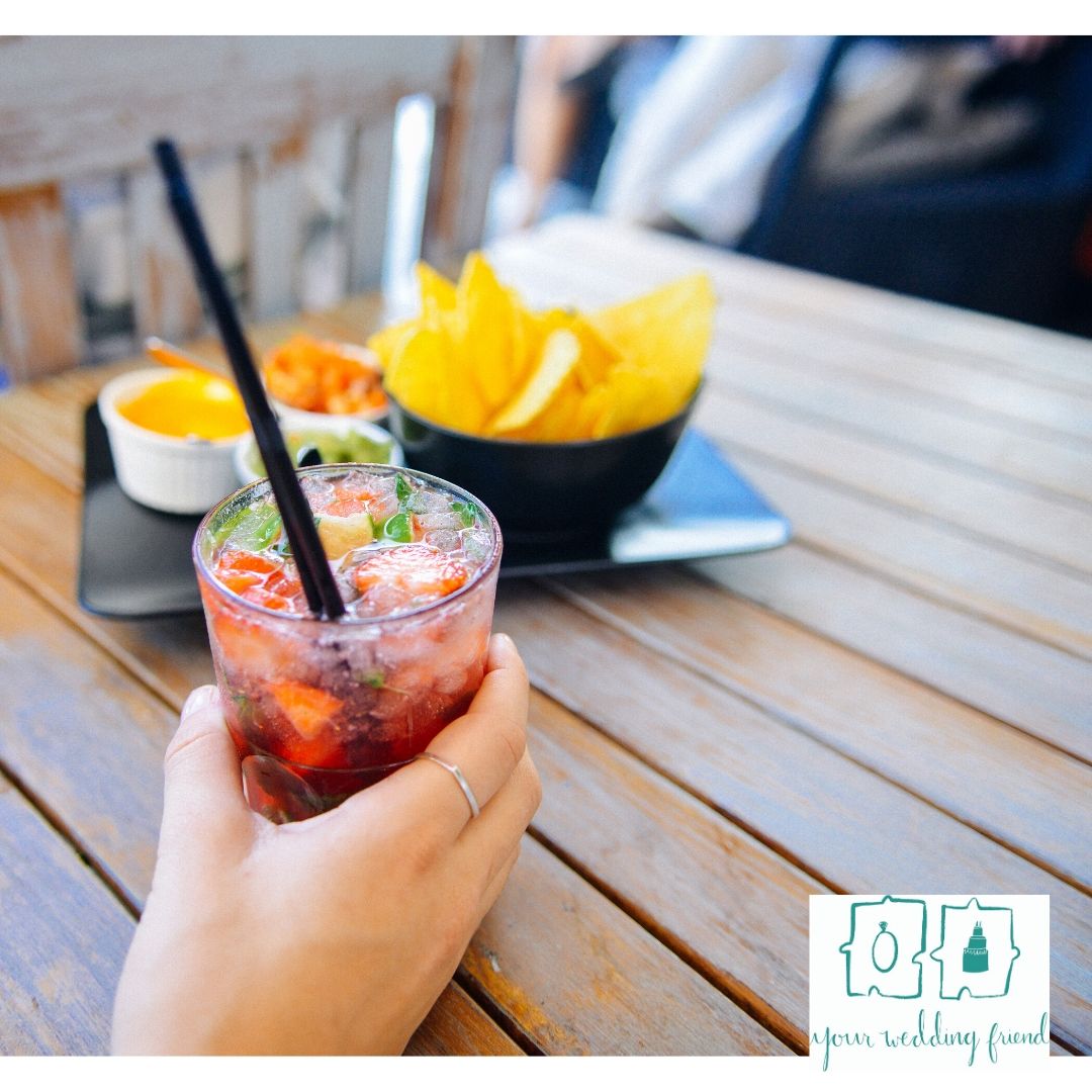 glass of ruit punch being held above a wodden tables with small bowls of snacks on it