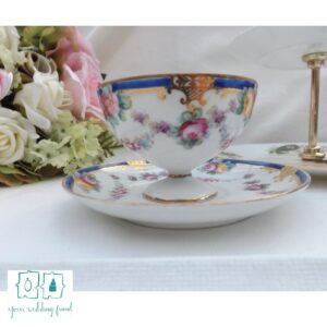 a fancy porceline tea cup and saucer sit on a white table cloth