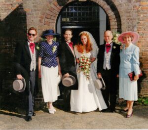 1996 wedding with bride dressed in ivory silk and groom is top hat and tails, with bride and grooms dads in matching outfits and the mums in blues, stood outside a church door